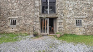 Un edificio de piedra con una entrada central, dos ventanas pequeñas a cada lado y un balcón con barandillas de metal.