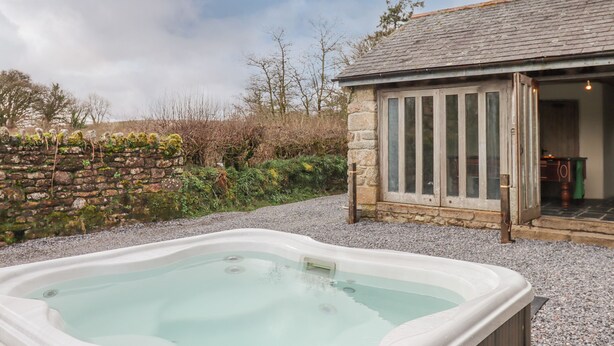 Un jacuzzi en un jardín con un muro de piedra y un edificio de madera al fondo.