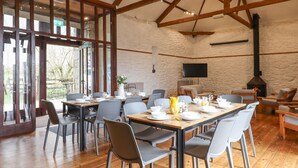 Un comedor con una mesa larga dispuesta para una comida, rodeada de sillas. Se observa una chimenea al fondo, y hay un televisor montado en la pared.