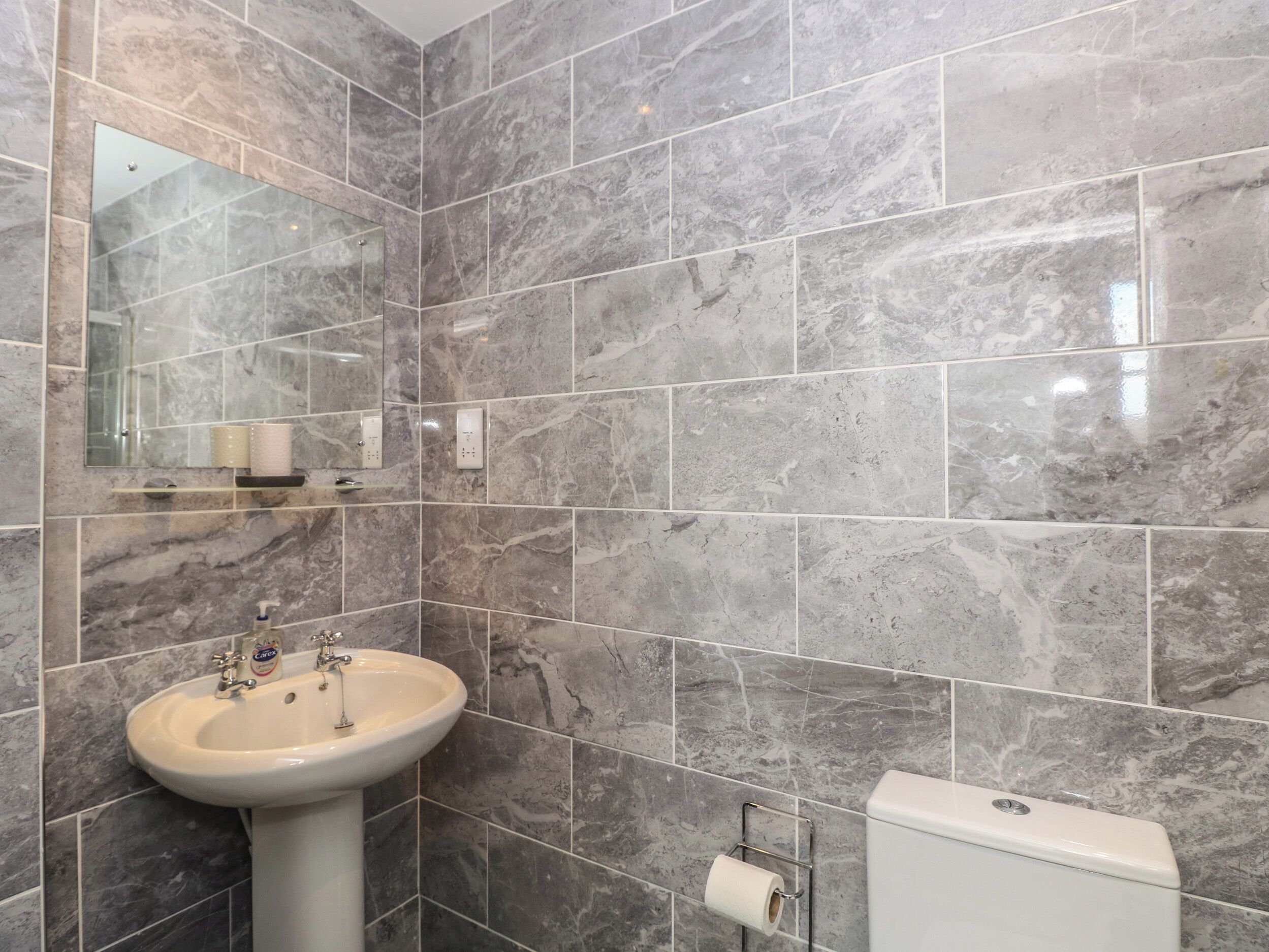 A bathroom with a marble wall, a sink, a mirror, and a toilet.