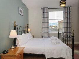A neatly made bed with white linens, a bedside lamp, and a window with plaid curtains.