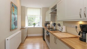 A modern kitchen with white cabinets, a wooden countertop, and a window with a view of greenery. - Baystones (Keswick)