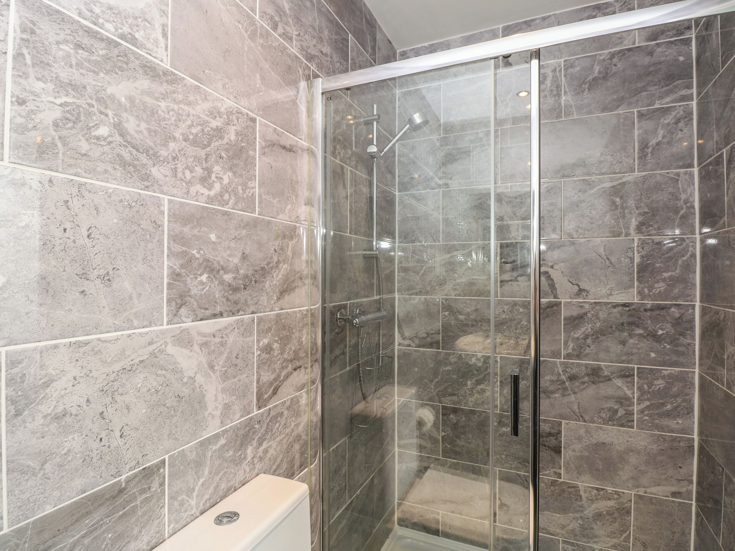 A modern bathroom with a glass-enclosed shower, marble tiles, and a toilet.