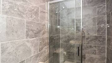 A modern bathroom with a glass-enclosed shower, marble tiles, and a toilet.