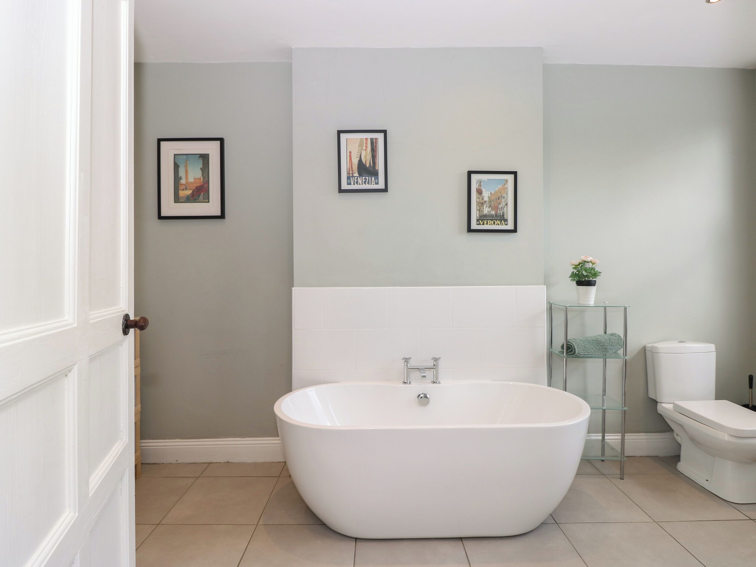 A modern bathroom with a freestanding bathtub, a toilet, and a glass shelf with a plant.