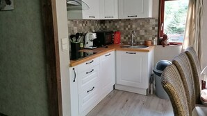 Una cocina compacta con armarios blancos, encimera de madera y ventana con cortinas.