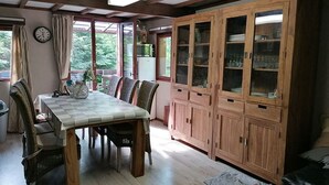 Un comedor con una mesa y sillas de madera, un mueble con puertas de vidrio y vistas a zonas verdes al exterior.