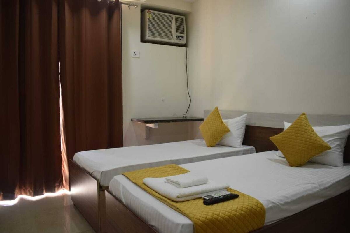 A hotel room with two single beds, each with a yellow pillow and a remote control on the bed.