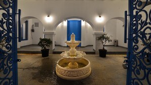 Un cortile con una fontana al centro, pareti bianche e una porta blu.