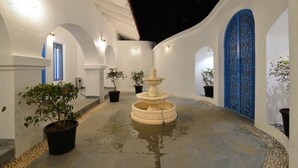 Un cortile con una fontana, piante in vaso e una porta decorativa blu.