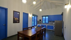 Zona pranzo con tavolo e sedie in legno, cucina con mobili blu e un frigorifero.