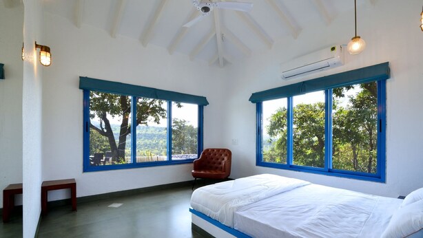 Una camera da letto con un letto, una sedia e due ampie finestre con cornici blu.
