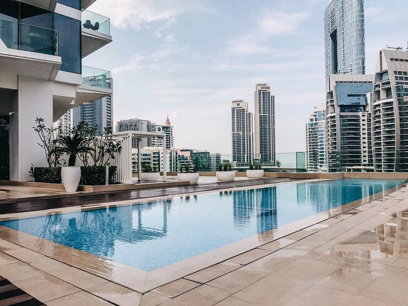 A rooftop pool with a cityscape view, modern buildings, and potted plants.