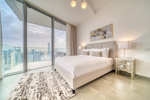 Quarto de hotel moderno com uma cama grande, vista para a cidade e porta de vidro que dá para uma varanda externa.
