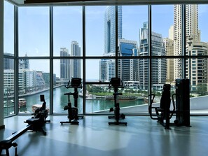Une salle de sport équipée de matériel d’exercice et dotée d’une grande fenêtre donnant sur un paysage urbain et une rivière.