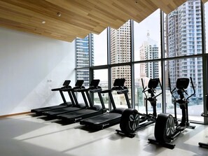 A modern gym with treadmills and a rowing machine, large windows offering city views.