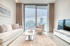 A modern living room with a sofa, armchair, TV, and a city view through large windows.