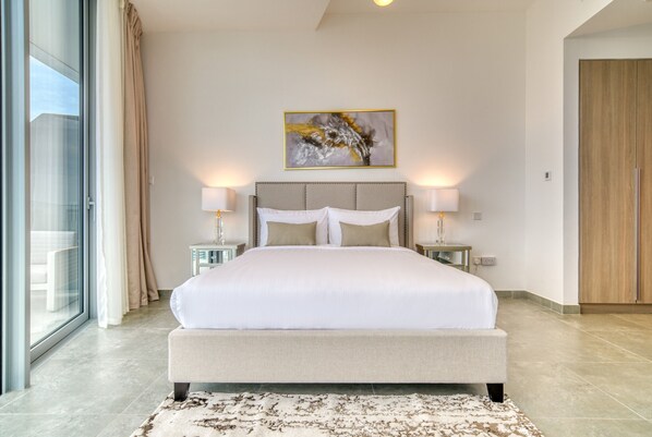 A spacious bedroom with a large bed, two bedside tables, and a large window with curtains.