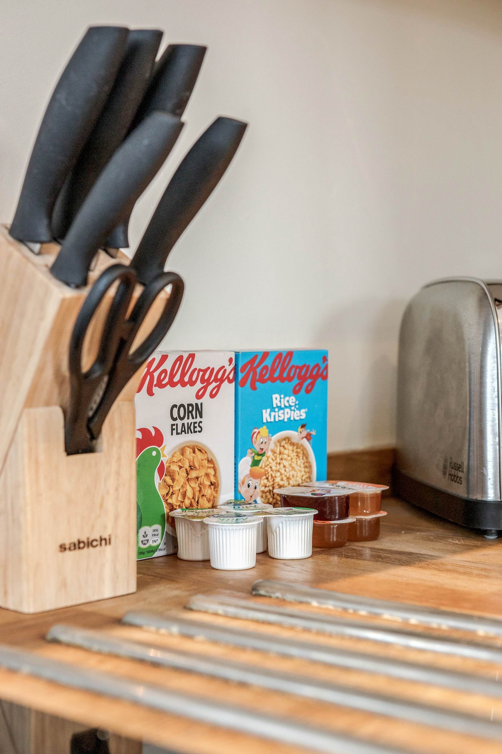 A kitchen counter with a knife block, a box of Kellogg's Corn Flakes, a box of Kellogg's Rice Krispies, and a toaster.