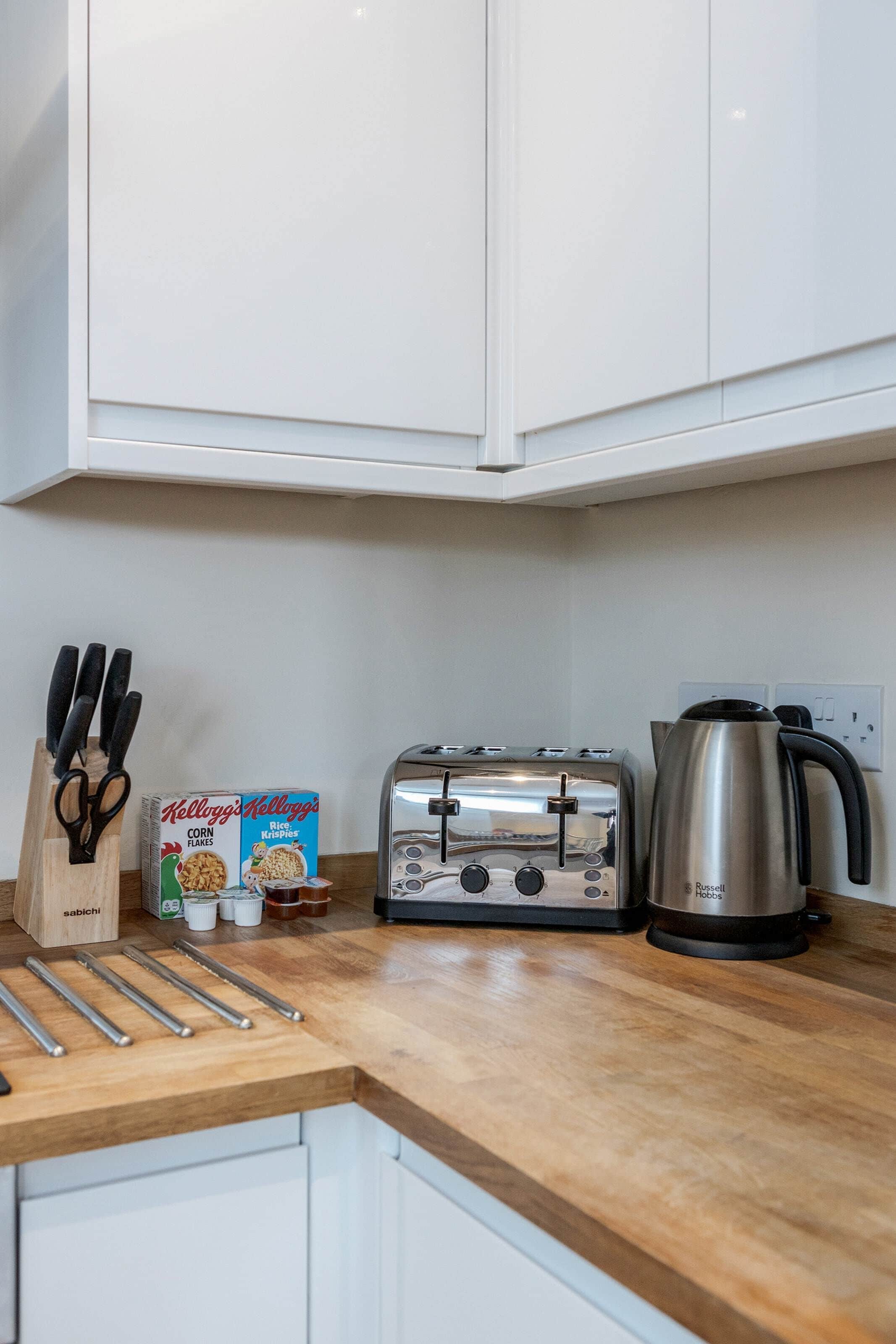 A kitchen with white cabinets, a toaster, a kettle, and a box of Kellogg's Corn Flakes.
