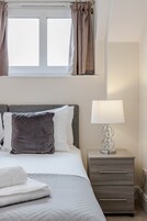 A bedroom with a bed, a bedside lamp, a nightstand, and a window with curtains.