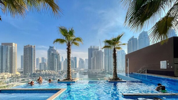 Ein Infinity-Pool auf dem Dach mit Palmen, umgeben von Hochhäusern.