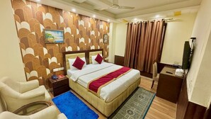 A hotel room with a bed, a desk, a chair, a blue rug, and a patterned rug. - Hotel Vista Inn (New Delhi)