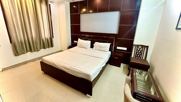 A modern bedroom with a large bed, a wooden headboard, a bedside table, and a chair. - Hotel Vista Inn (New Delhi)