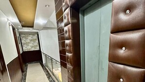A hallway with marble flooring, a brown leather wall, and a green elevator door. - Hotel Vista Inn (New Delhi)