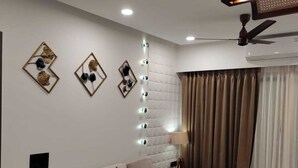 A modern living room with a sofa, a dining table with placemats, decorative wall art, recessed ceiling lights, and an air conditioning unit. - Goan Fiesta Ultra Luxury Suite Calangute (Calangute)
