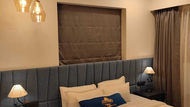 A hotel room with a bed, nightstands, a ceiling fan, and a large window with curtains. - Goan Fiesta Ultra Luxury Suite Calangute (Calangute)