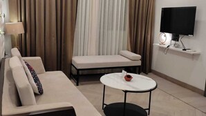 A modern living room with a sofa, a coffee table, a TV, and an air conditioning unit. - Goan Fiesta Ultra Luxury Suite Calangute (Calangute)