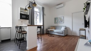 Eine moderne Küche mit integriertem Mikrowellenherd, einem Essbereich mit Tisch und Stühlen, einem grauen Sofa und einem kleinen Beistelltisch.