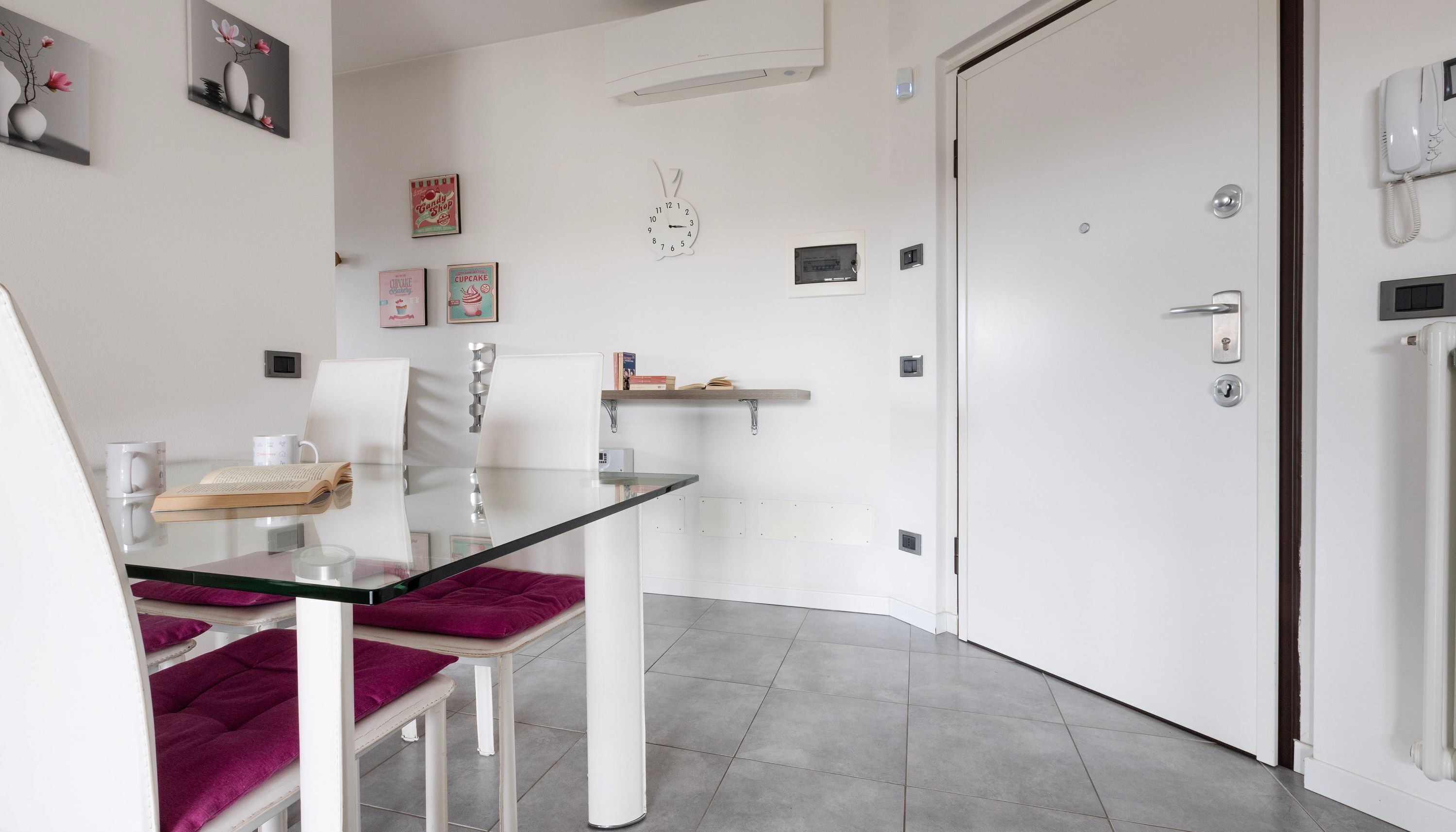 A modern kitchen with a glass table, white chairs, and a white door.