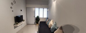 A modern bedroom with a bed, a TV on a shelf, a potted plant, and a door leading to another room. - Margosa A Stay Botani Ipoh Homestay 3 BR (Ipoh)
