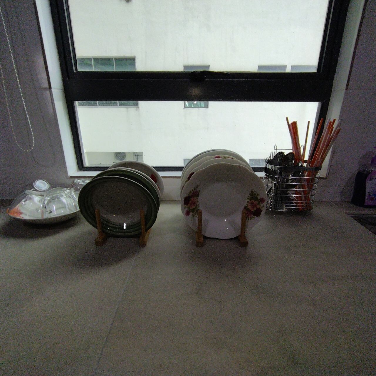 A kitchen counter with stacked plates, a dish rack, and a utensil holder.