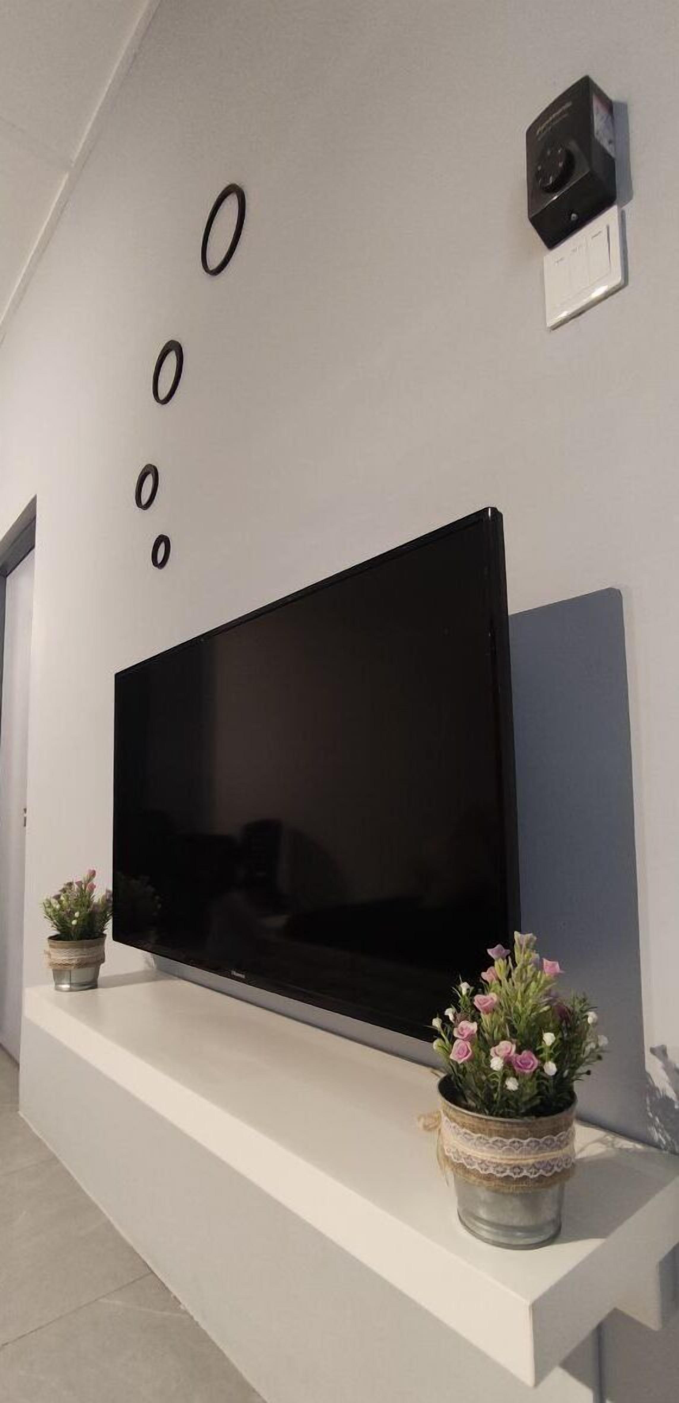 Ein Flachbildfernseher ist an einer weißen Wand mit minimalistischem Design angebracht, zusammen mit einem Lautsprecher und dekorativen Kreisen darüber.