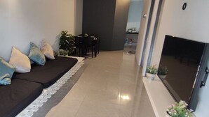 Una sala de estar moderna con un sofá negro, varios cojines, una mesita y un televisor.