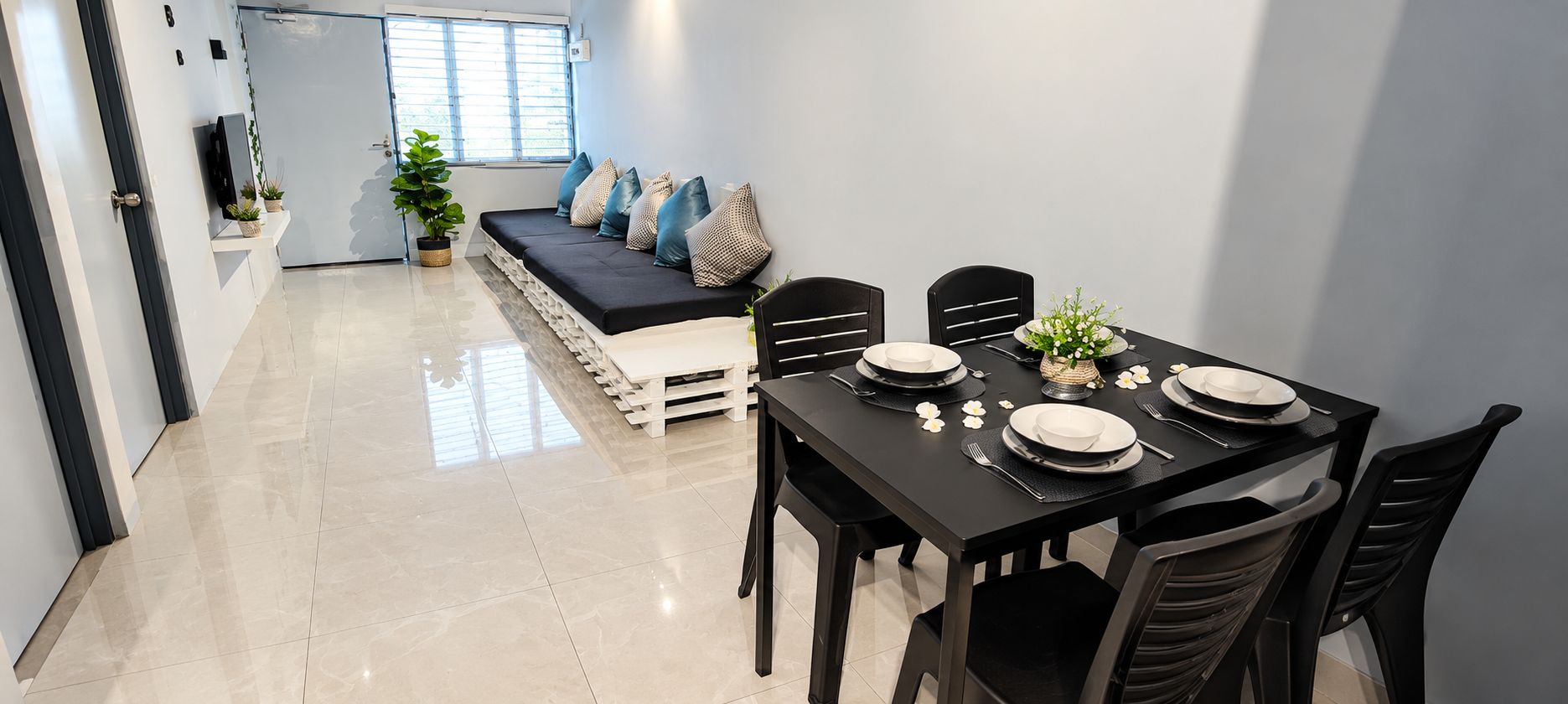 Comedor con mesa negra para cuatro, platos blancos y sofá negro con cojines.