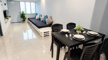 Comedor con mesa negra para cuatro, platos blancos y sofá negro con cojines.
