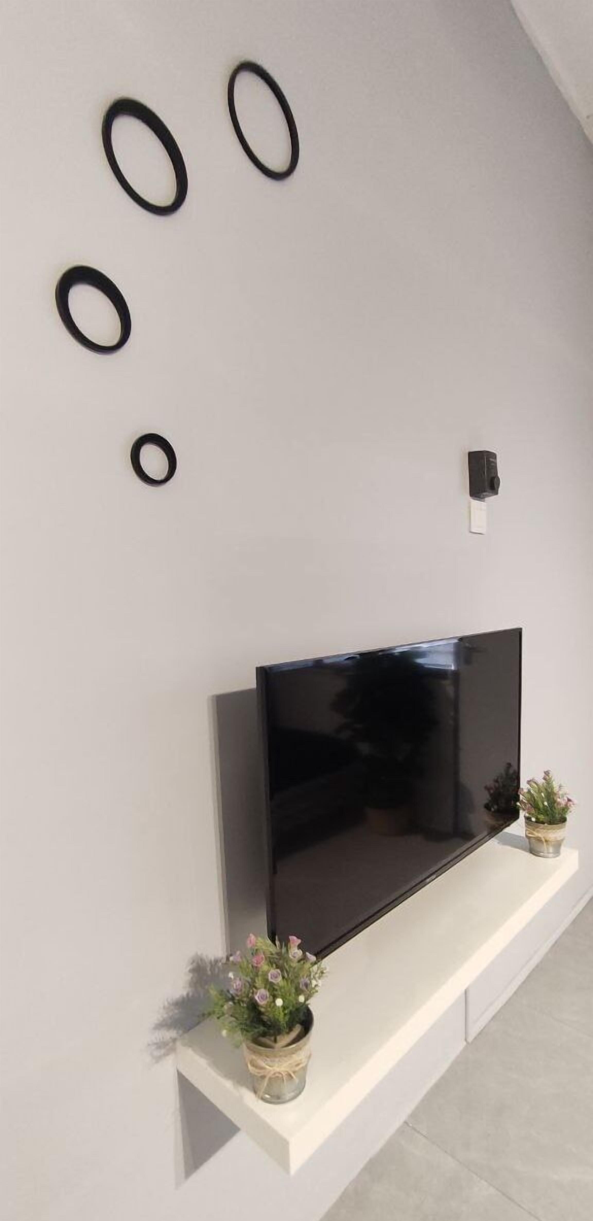 A modern living room with a flat-screen TV mounted on a white wall, a white console table below, and three black circular wall decorations.