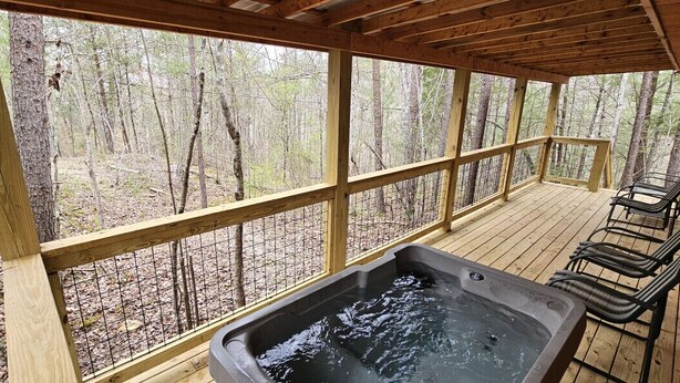 Eine Holzterrasse mit Whirlpool und Stühlen, umgeben von einem Hollergazier und Blick ins Waldgebiet.