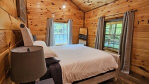Ein Schlafzimmer einer Holzhütte mit einem Bett, einer Lampe und zwei Fenstern.