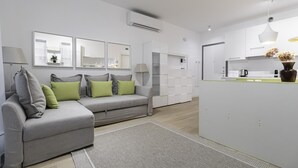 A modern living room with a grey sofa, green cushions, a grey rug, and a kitchen area with white cabinets and a coffee machine. - Italianway Comfort - Compagnoni 12 - Suite Mirabel (Milan)