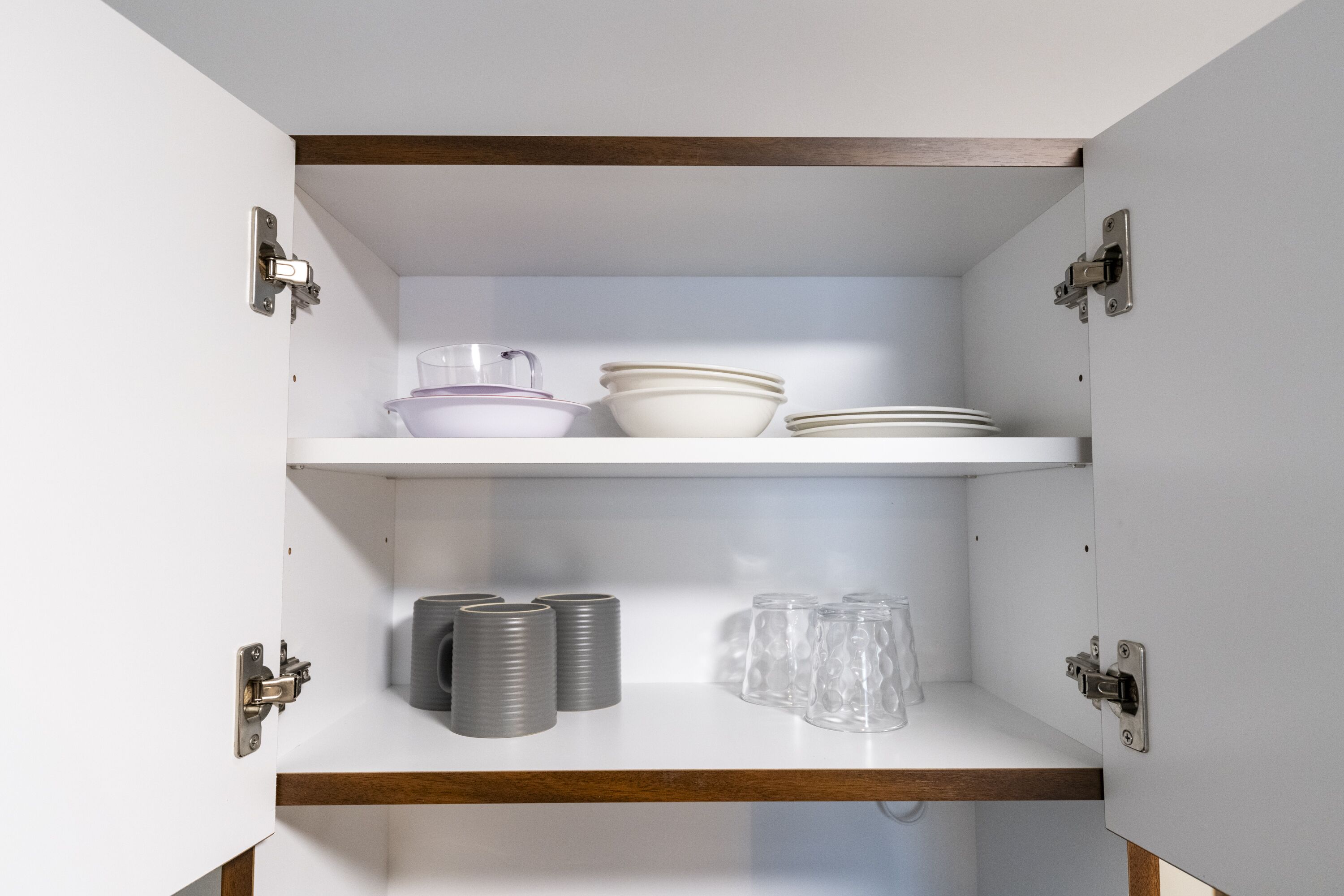 Un mueble de cocina con dos repisas, una con cuencos y la otra con tazas y platos.