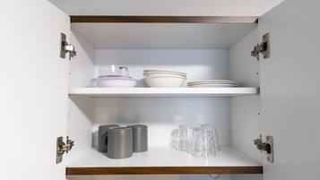 Un mueble de cocina con dos repisas, una con cuencos y la otra con tazas y platos.