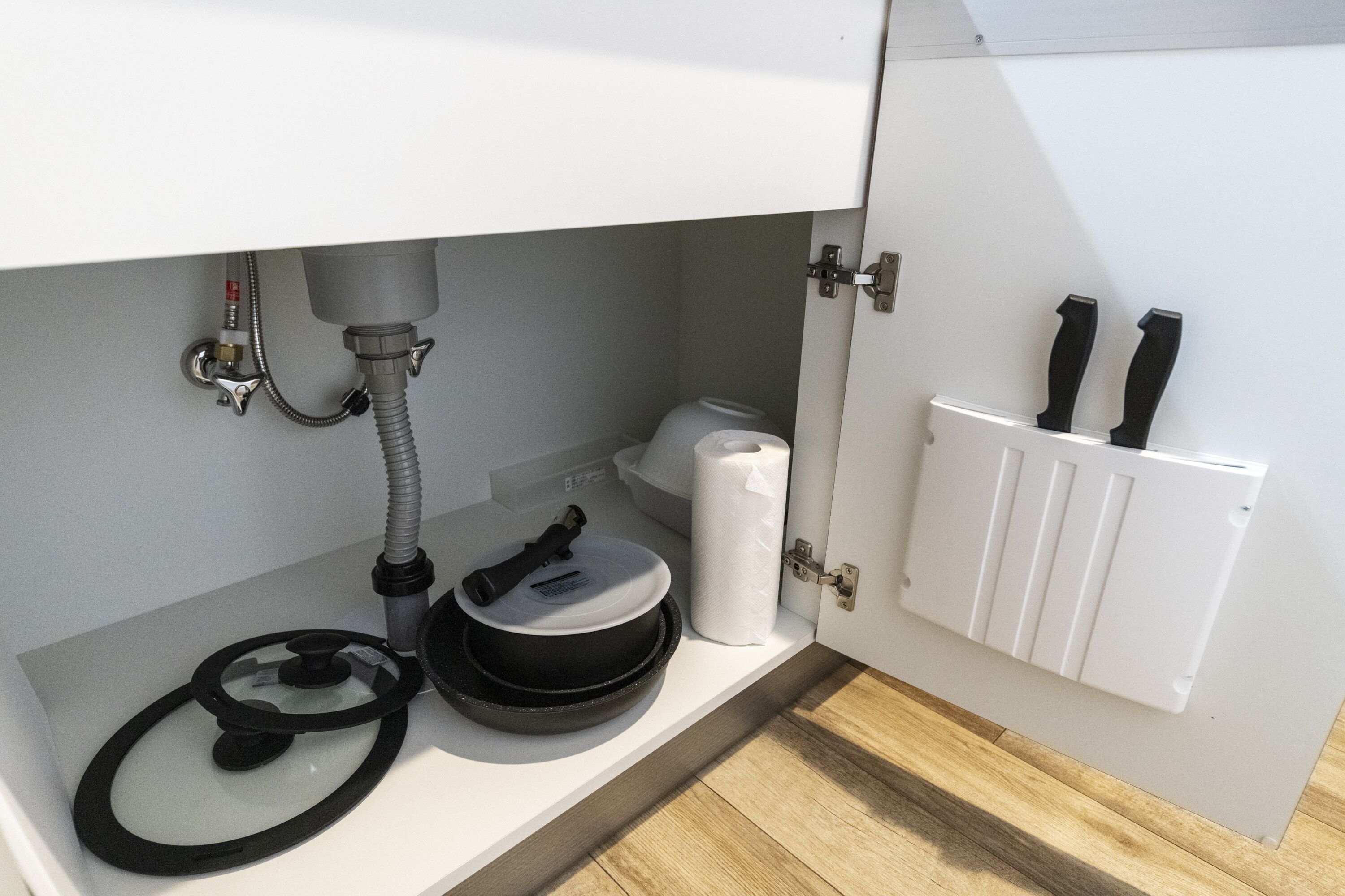 A kitchen with a white countertop, a black pan, a roll of paper towels, a white radiator, and a black hose.