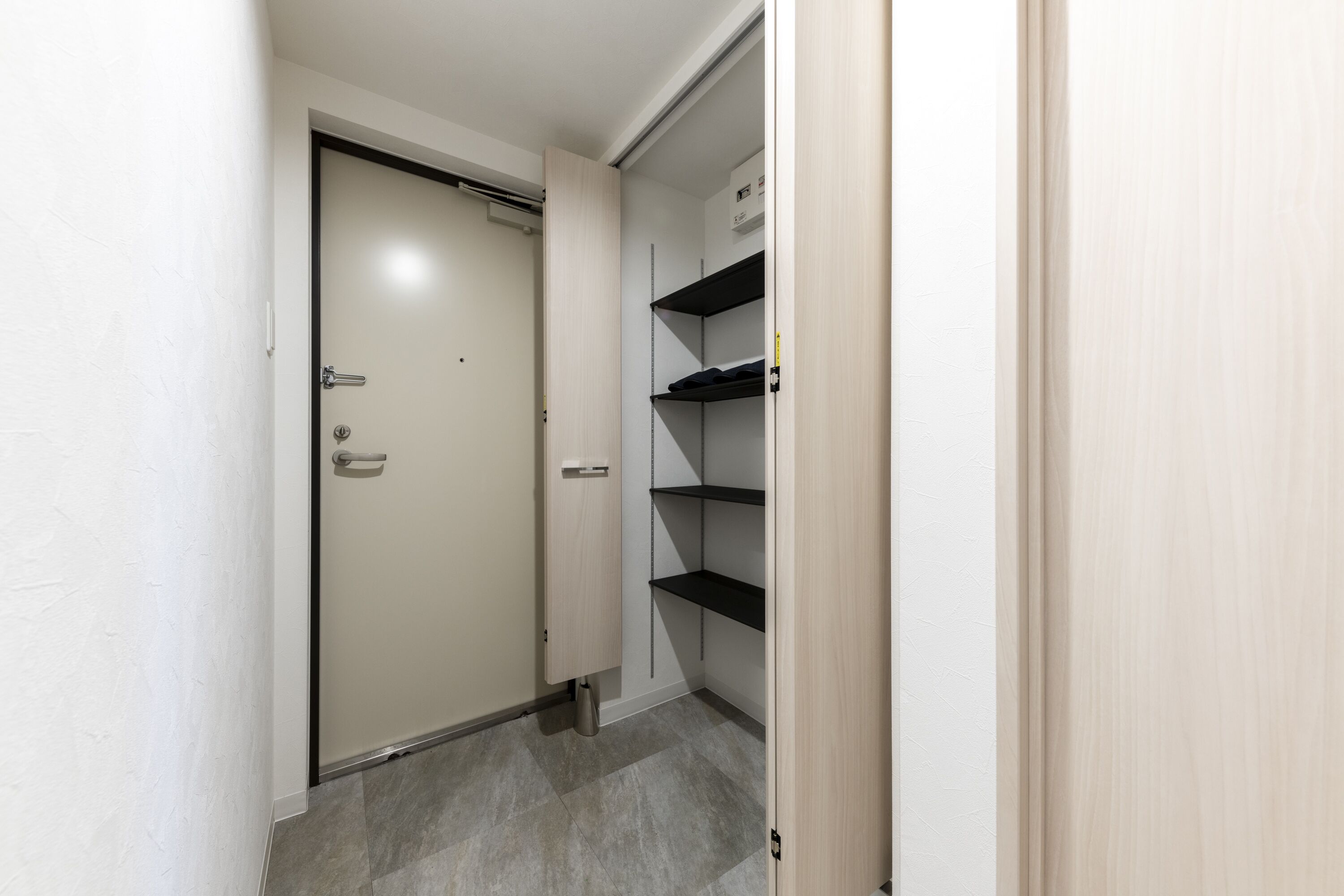 A narrow hallway with a closed door, a metal shelf unit with a few items, and a trash bin.