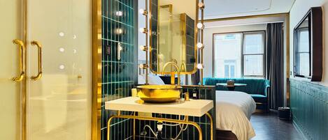 Une salle de bain d’hôtel comprenant un meuble-lavabo, un grand miroir avec éclairage, un lavabo et un espace douche.