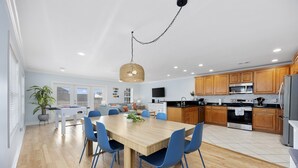 Une cuisine moderne avec des meubles en bois, un réfrigérateur en acier inoxydable et un coin repas comprenant une table en bois et des chaises bleues.